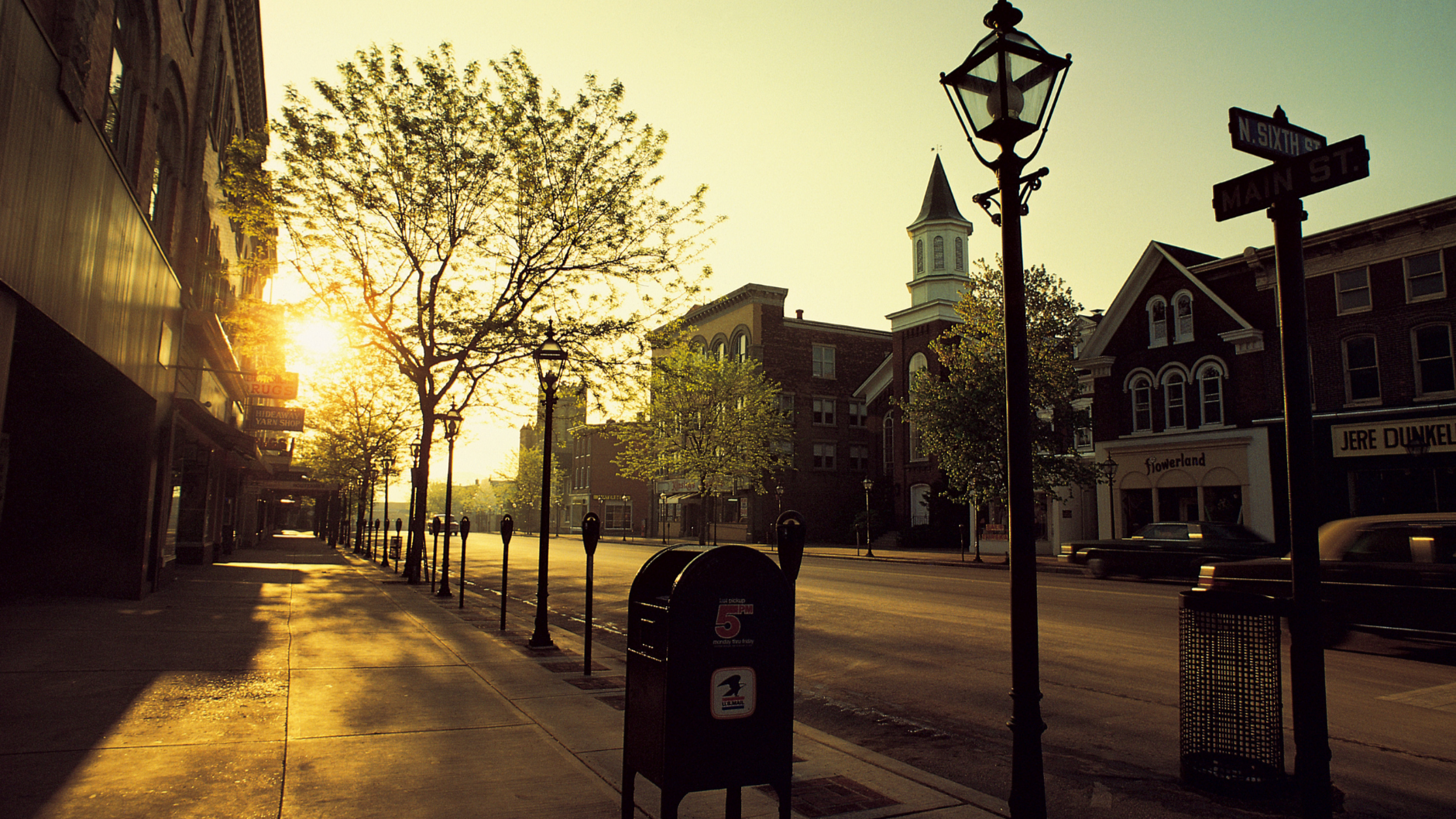 City street with sunset casting a warm glow, featuring a mailbox and street lamp.