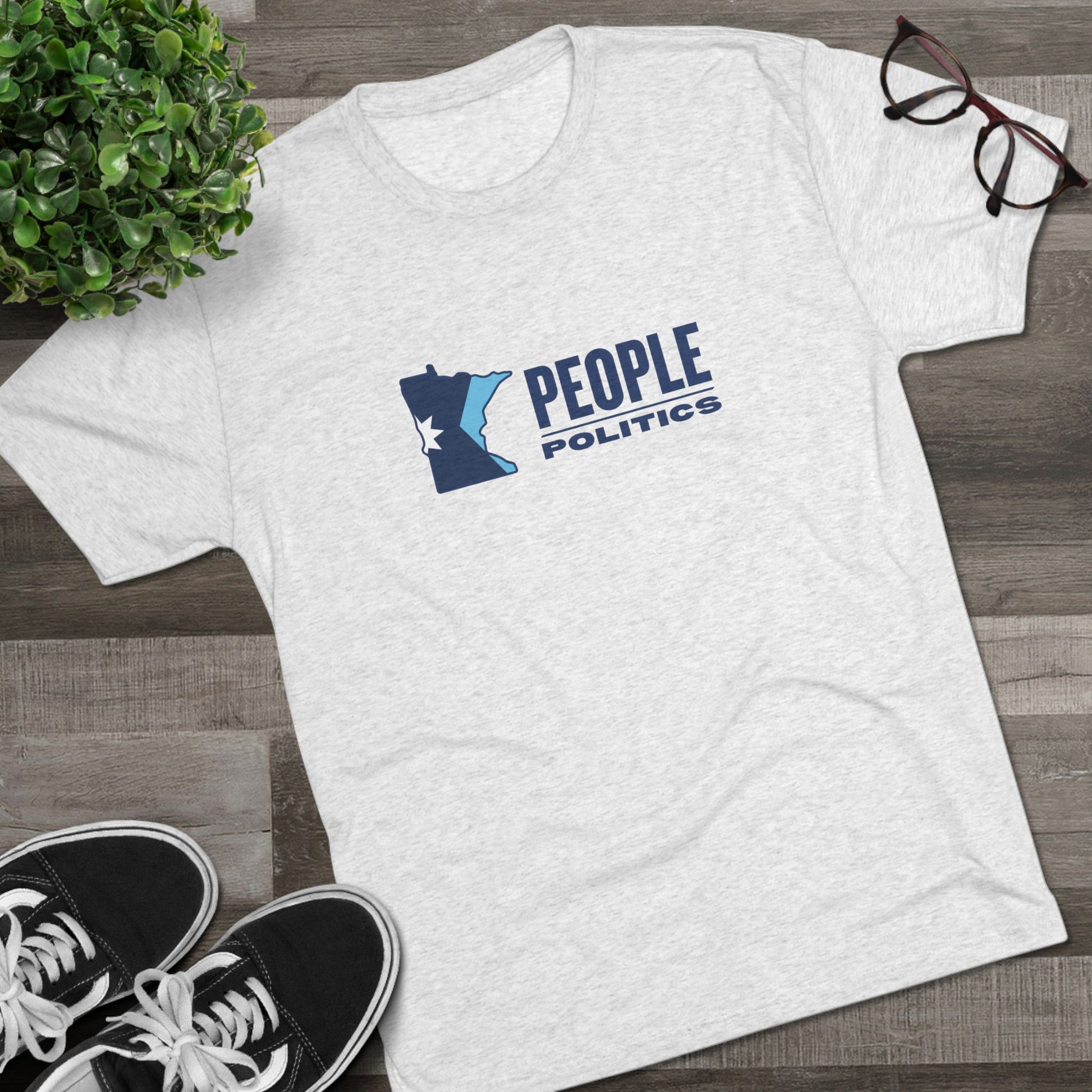 White t-shirt with 'People Over Politics' graphic on a wooden surface with shoes and glasses.