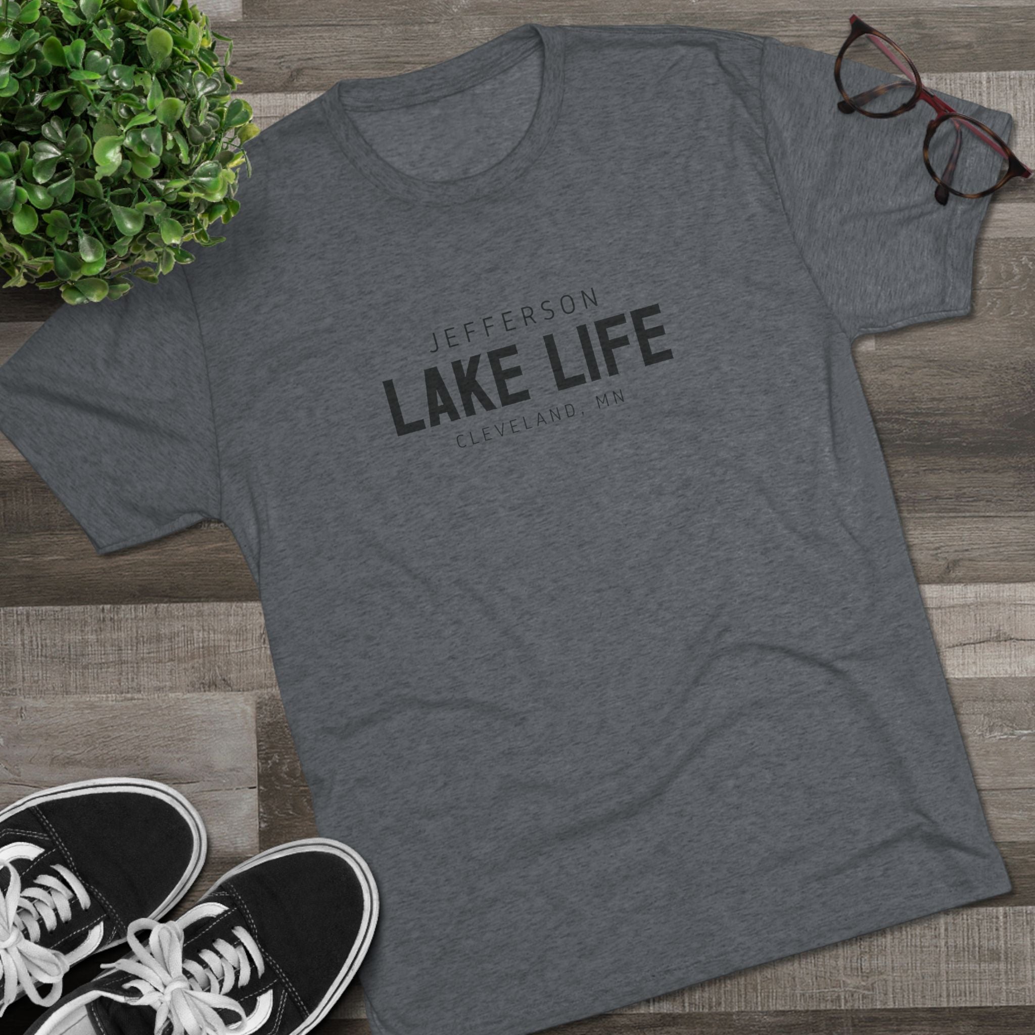 Gray t-shirt with 'Jefferson Lake Life' text on a wooden surface with sneakers and a plant.