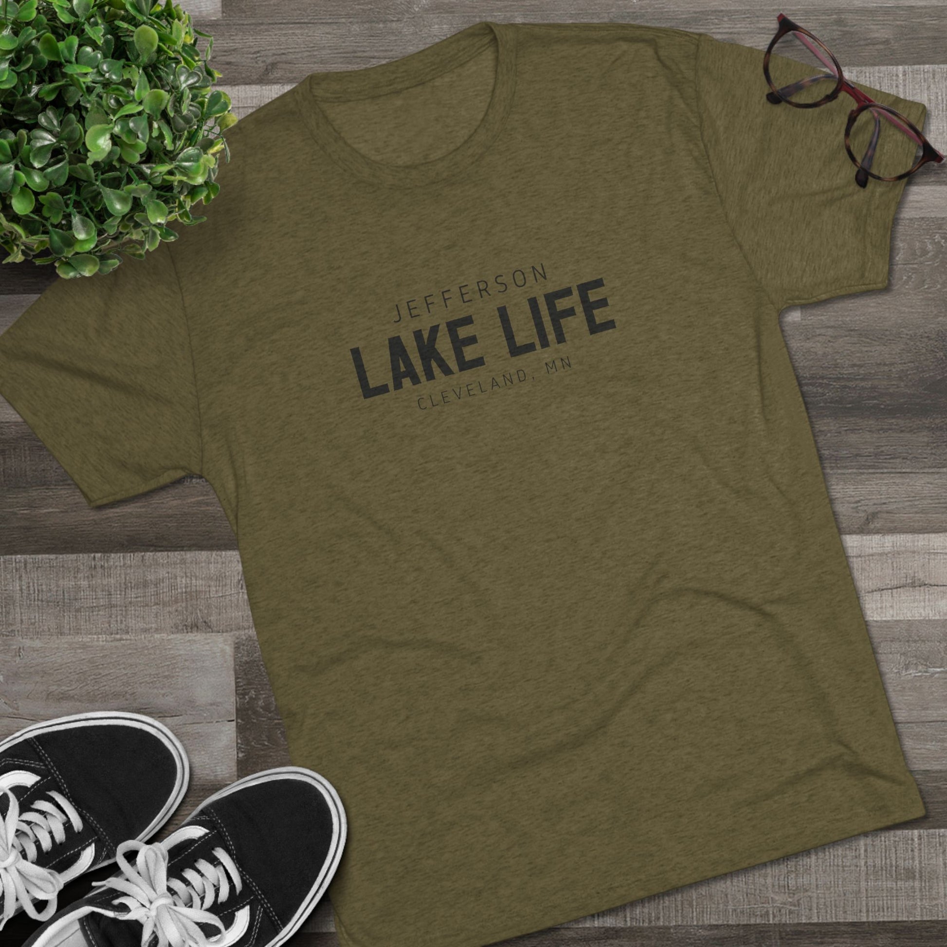 Green t-shirt with 'Jefferson Lake Life' text on a wooden surface with sneakers and glasses.