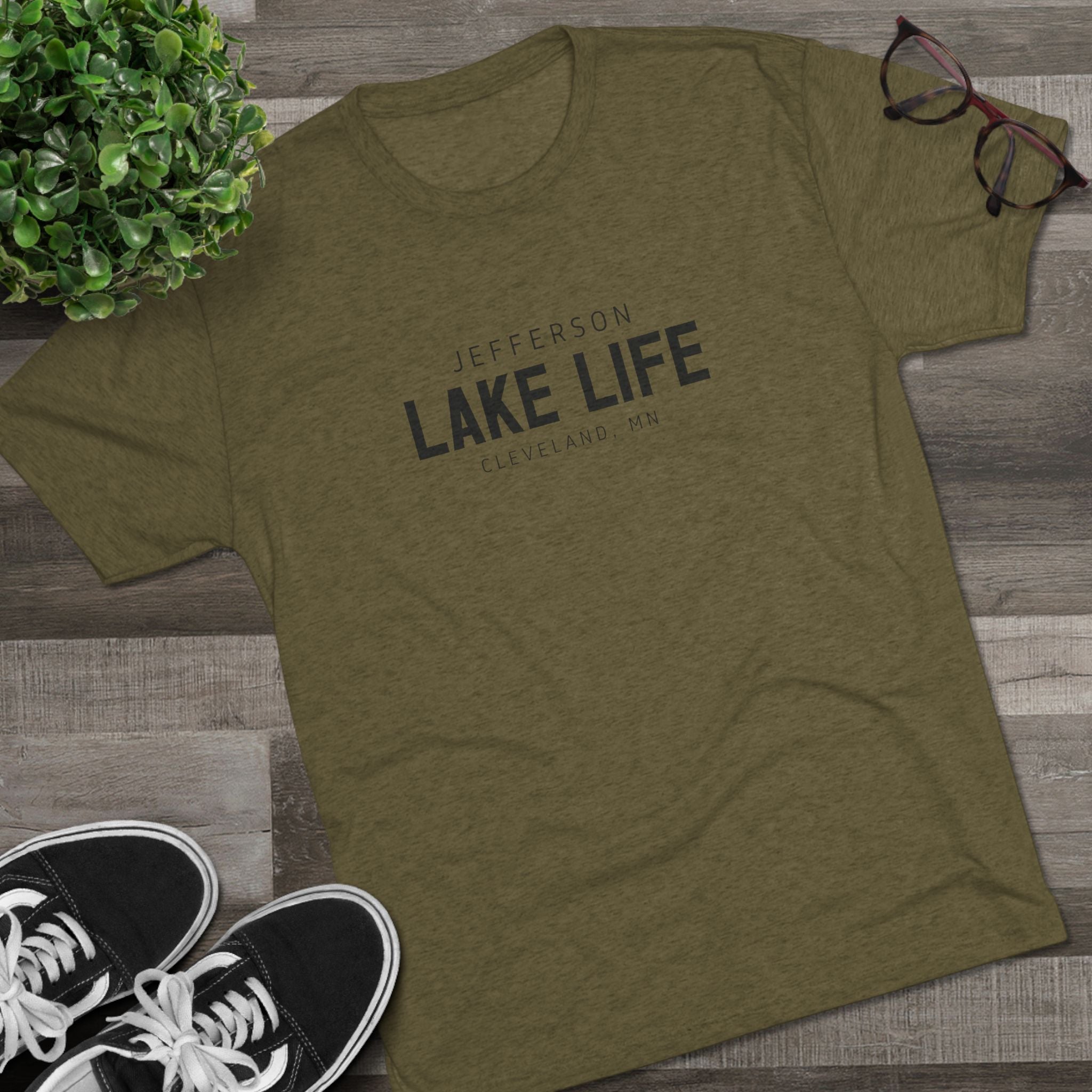 Green t-shirt with 'Jefferson Lake Life' text on a wooden surface with sneakers and glasses.