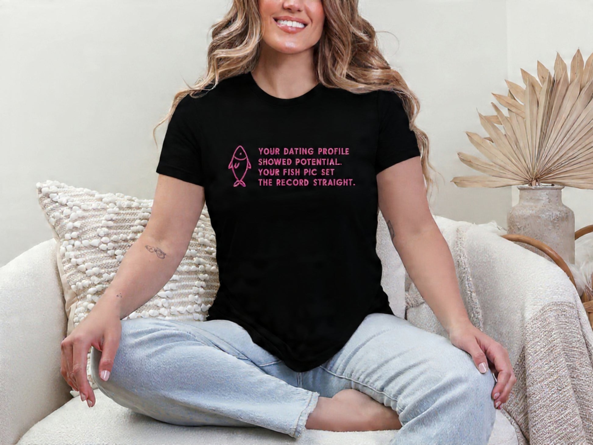 Woman wearing a black t-shirt with pink text sitting on a couch.